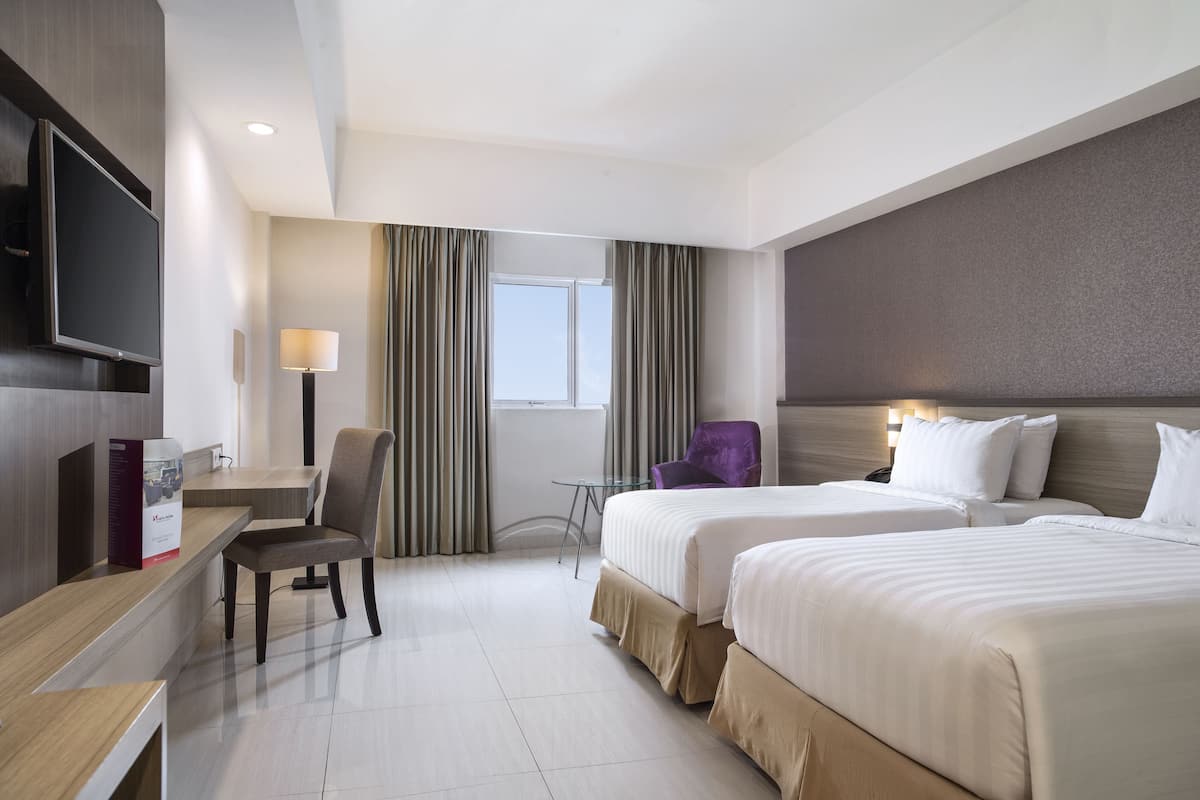Une chambre d’hôtel avec deux lits, un bureau, une chaise, une télévision et une fenêtre avec des rideaux.