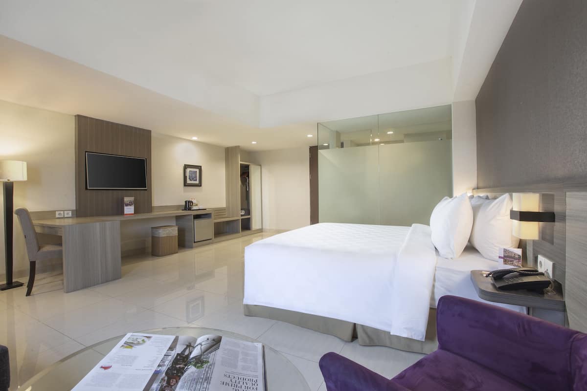 Une chambre d’hôtel équipée d’un lit, d’un bureau, d’une chaise, d’une télévision et d’une table en verre sur laquelle se trouve un magazine.