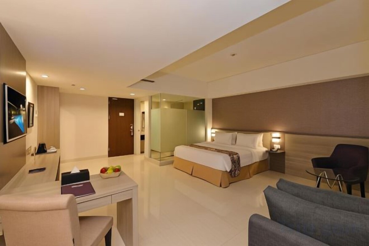 A modern hotel room with a bed, a desk, a chair, a TV, and a bathroom.