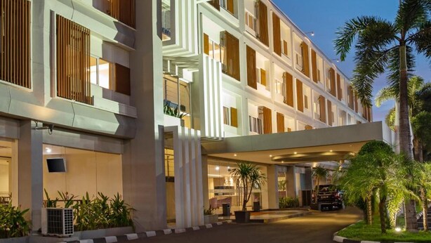 A modern hotel with multiple floors, a covered entrance, and a landscaped area with palm trees.