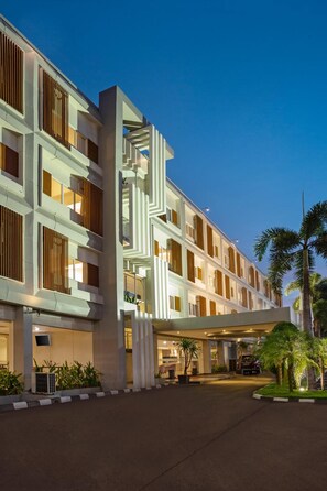 Un hôtel moderne à plusieurs étages, doté d’une entrée couverte et d’un espace paysager agrémenté de palmiers.
