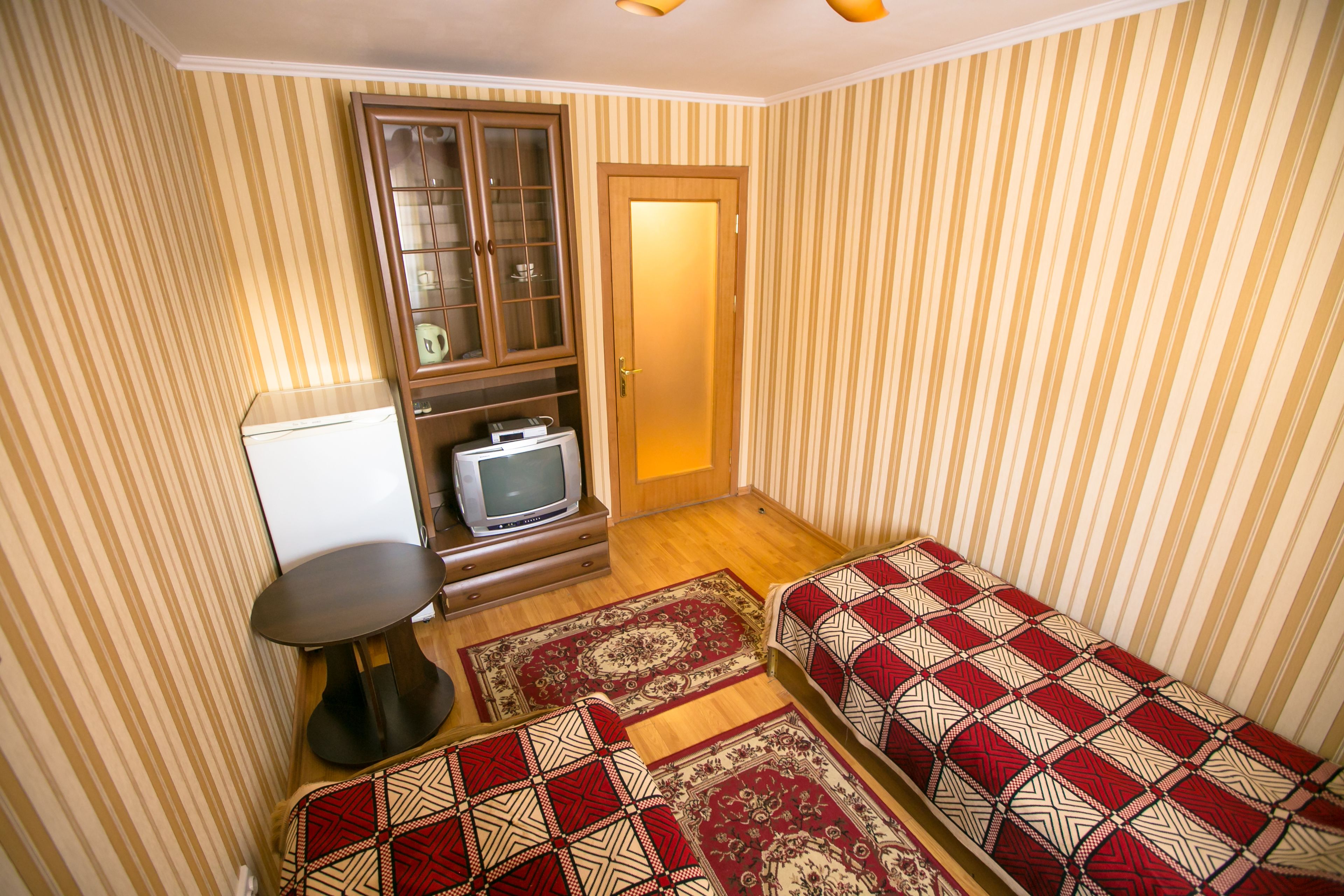 A compact living space with striped wallpaper, a wooden cabinet with glass doors, a television, and two patterned sofas.