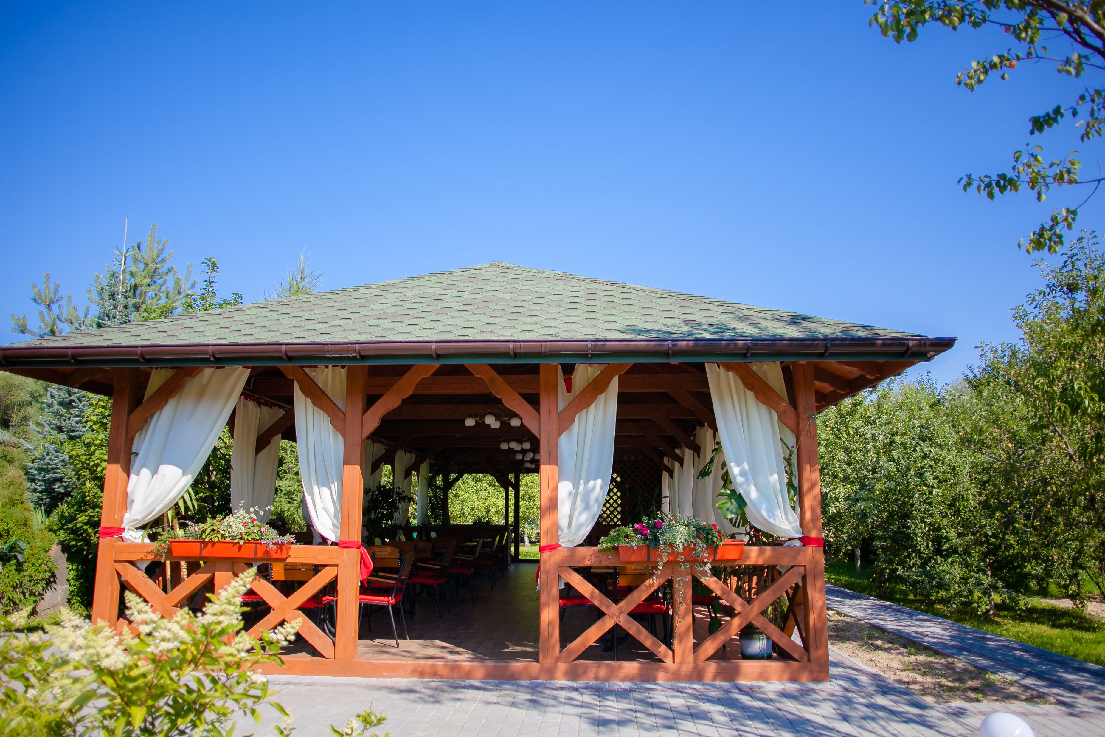 A wooden pavilion with a tiled roof, surrounded by greenery and trees.
