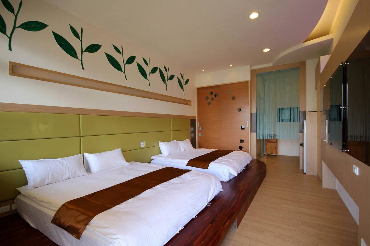 Quarto de hotel com duas camas, cabeceira de madeira, um espelho grande e uma parede decorada com folhagens.