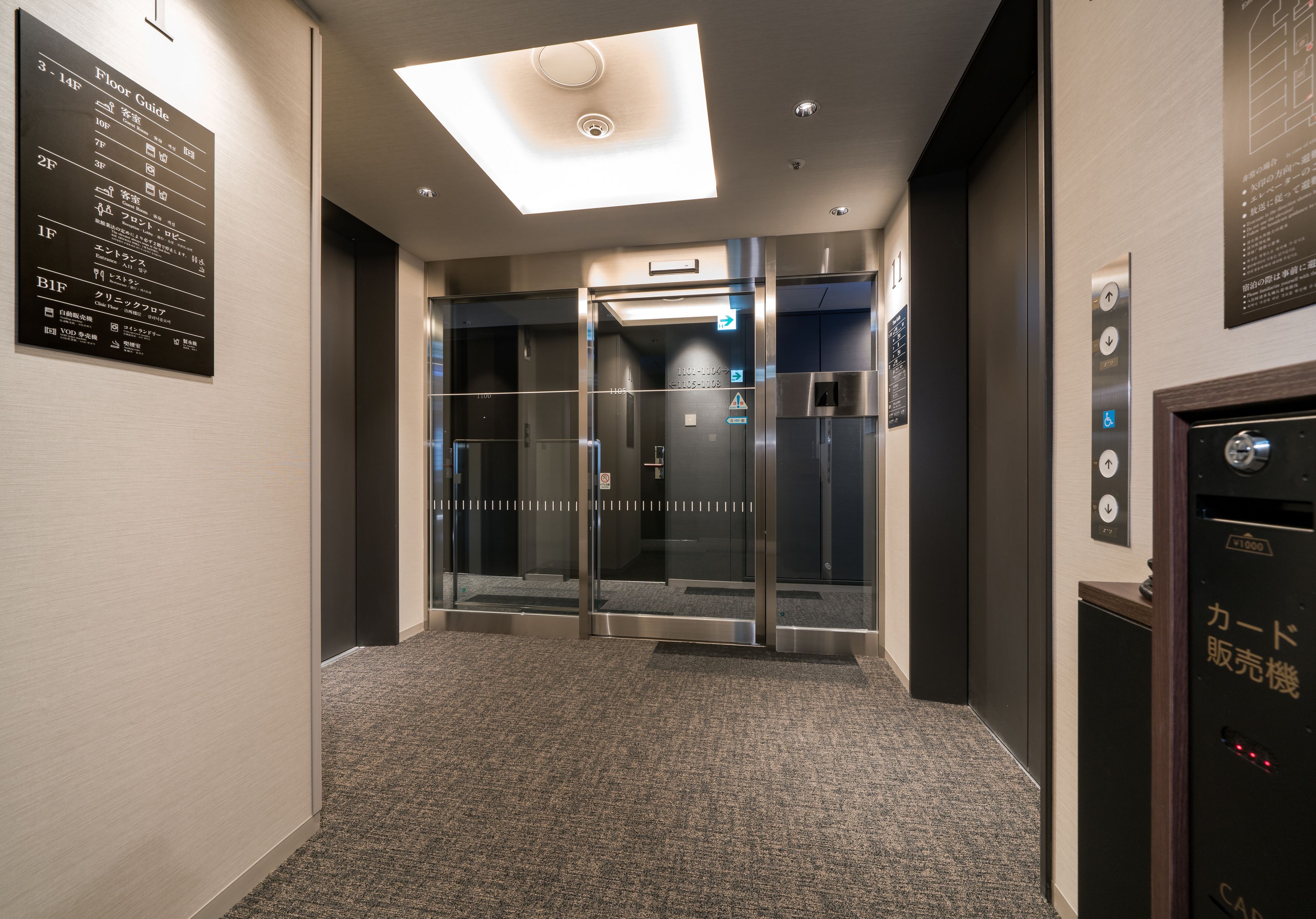 An elevator area with a floor guide sign, a card vending machine, and a glass elevator door.