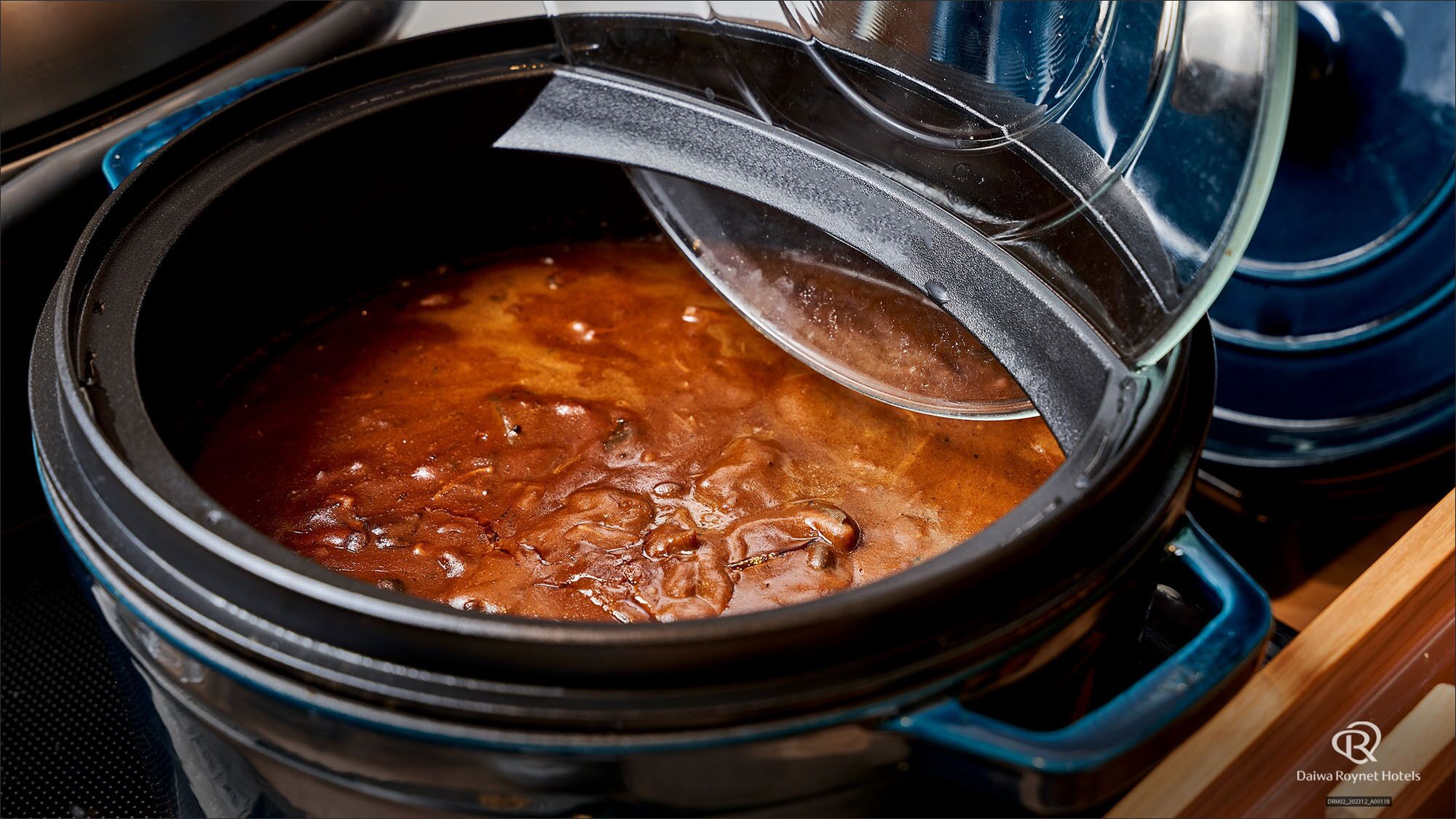 A slow cooker with a lid partially open, revealing a bubbling stew or soup.