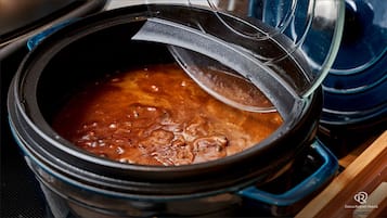 A slow cooker with a lid partially open, revealing a bubbling stew or soup.