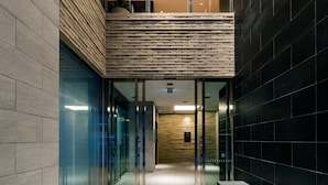 A modern interior with a glass elevator, a mezzanine level, and a black tiled wall.