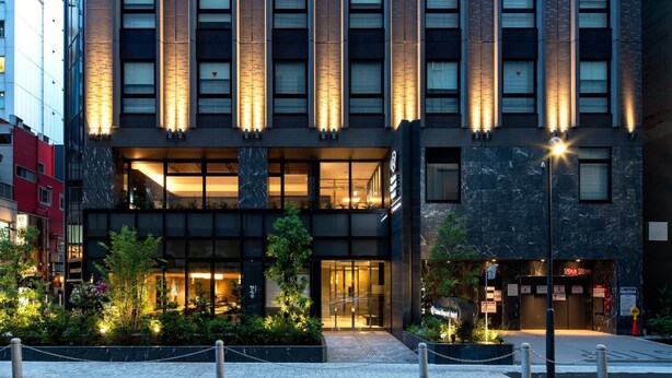 A modern building with a glass entrance, a well-lit facade, and a landscaped courtyard.