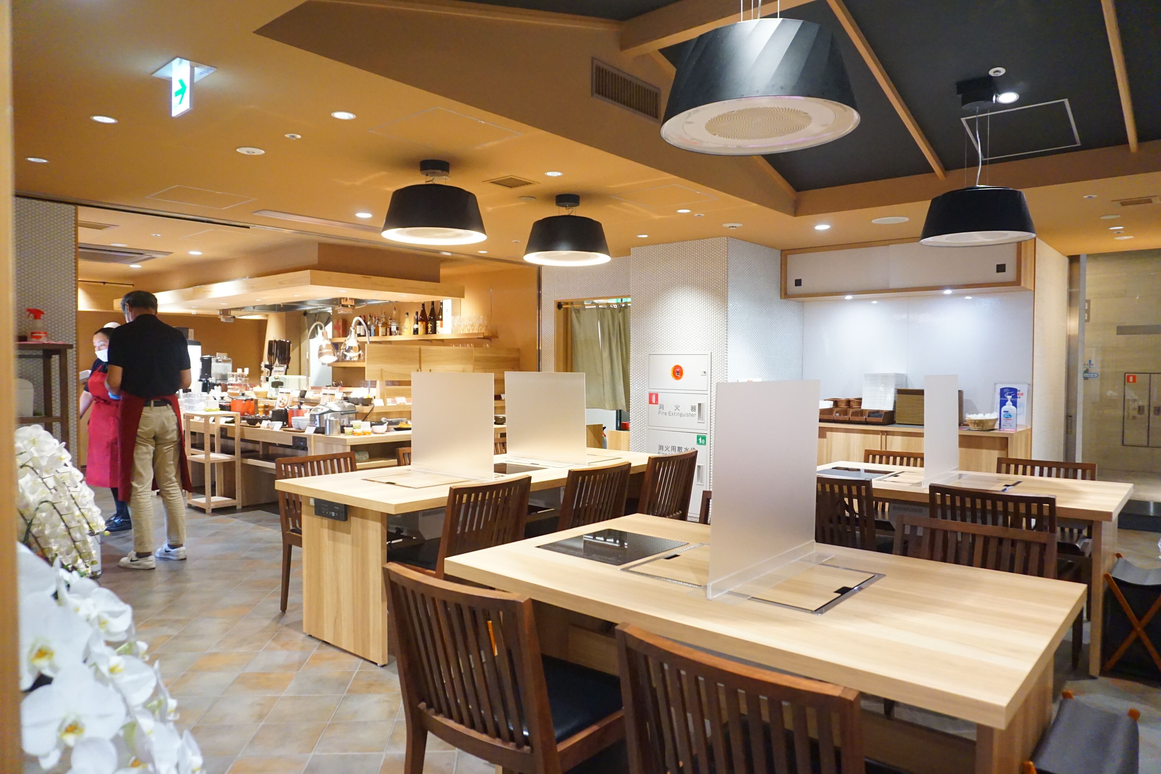 Un restaurante moderno con mesas y sillas de madera, una zona de cocina y un extintor visible.