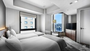 A modern hotel room with two beds, a television, a desk, and a large window offering a city view.