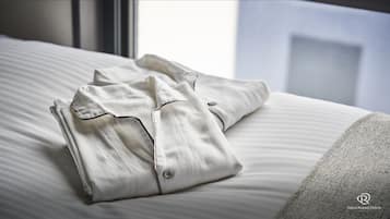 Du linge de lit blanc, soigneusement plié, est posé sur un lit, avec une fenêtre en arrière-plan.