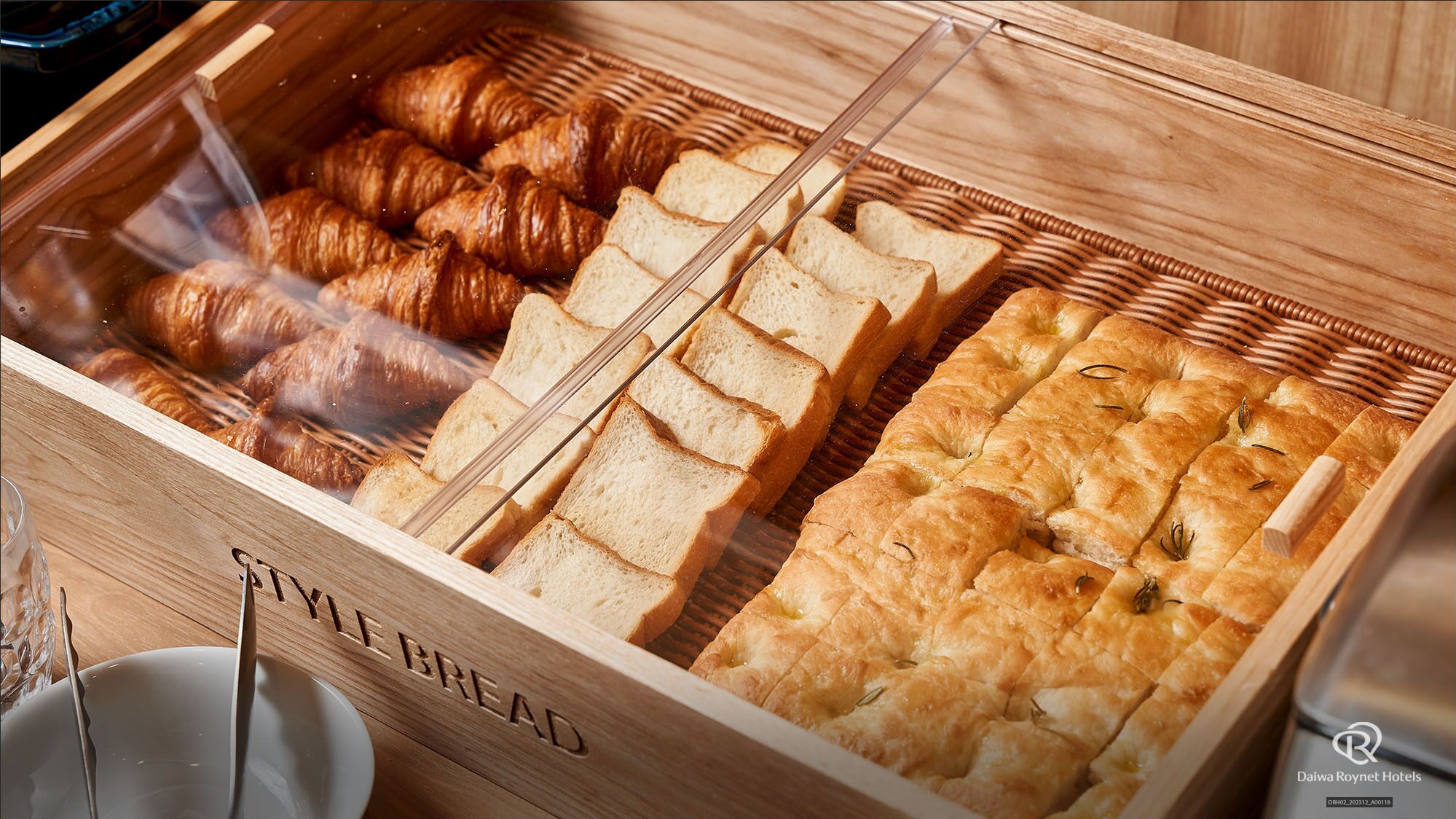 A bakery display case with croissants, sliced bread, and a loaf of bread with herbs.