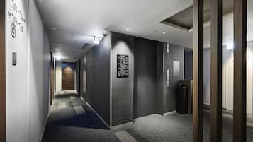 A modern hotel hallway with a carpeted floor, a digital elevator display, and a security camera.