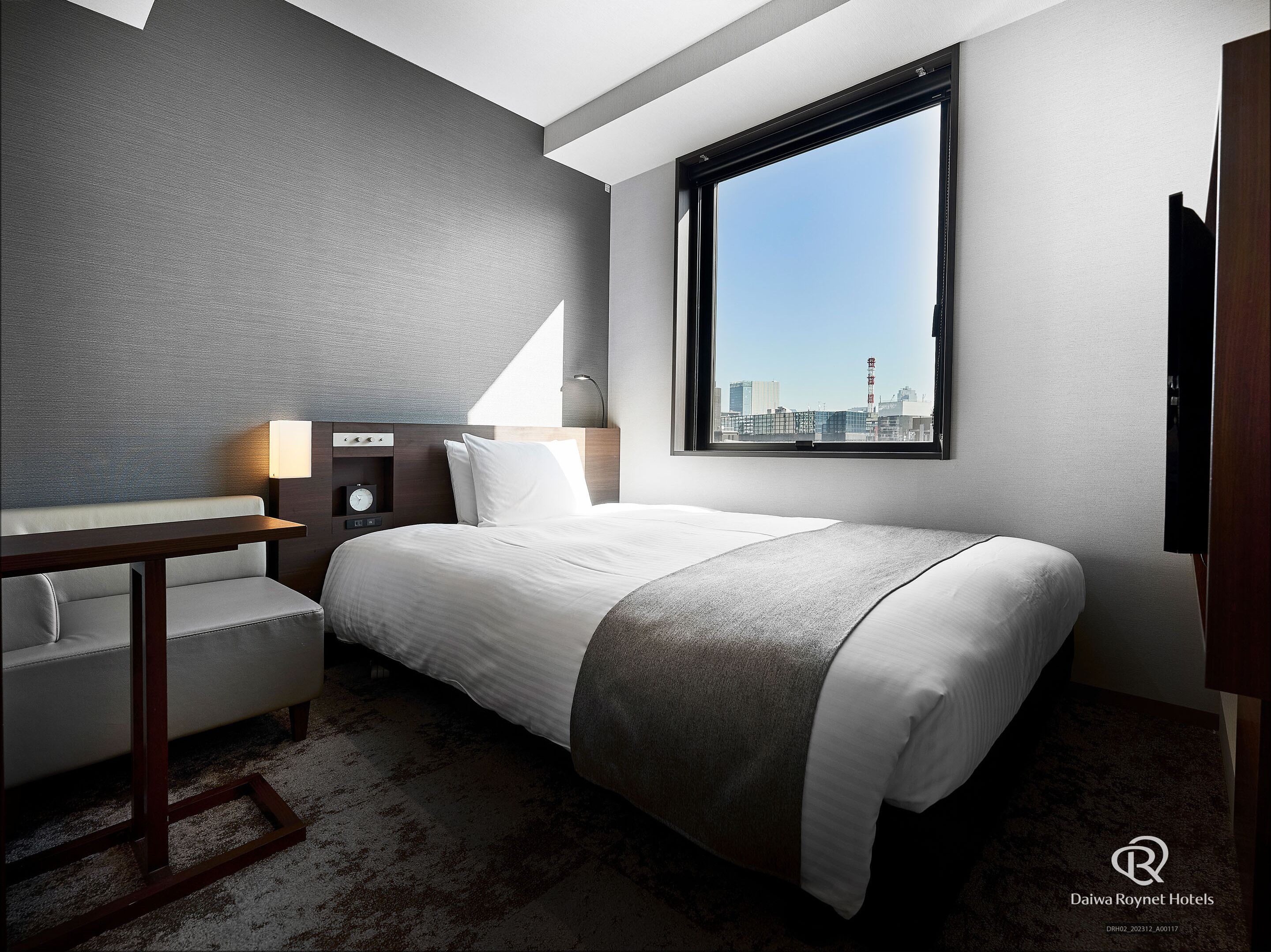 A hotel room with a bed, a desk, a lamp, and a view of the city skyline.