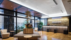 A modern hotel lobby with a reception desk, seating area, and large windows.