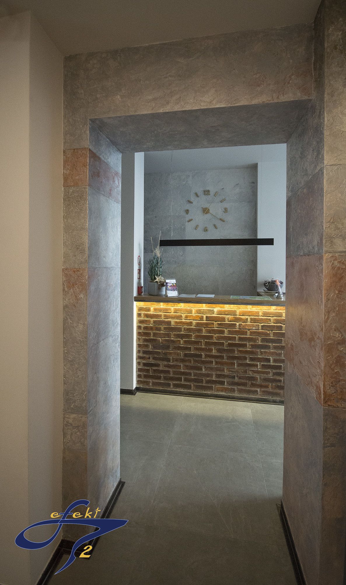Un espace d’accueil avec un mur en briques, une horloge et un comptoir d’accueil.