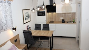 Angolo cottura compatto con zona pranzo, tavolo e sedie in legno.