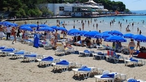 Una spiaggia con numerosi ombrelloni blu e lettini bianchi.