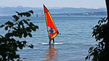 Una persona practica windsurf en un lago, con montañas al fondo.