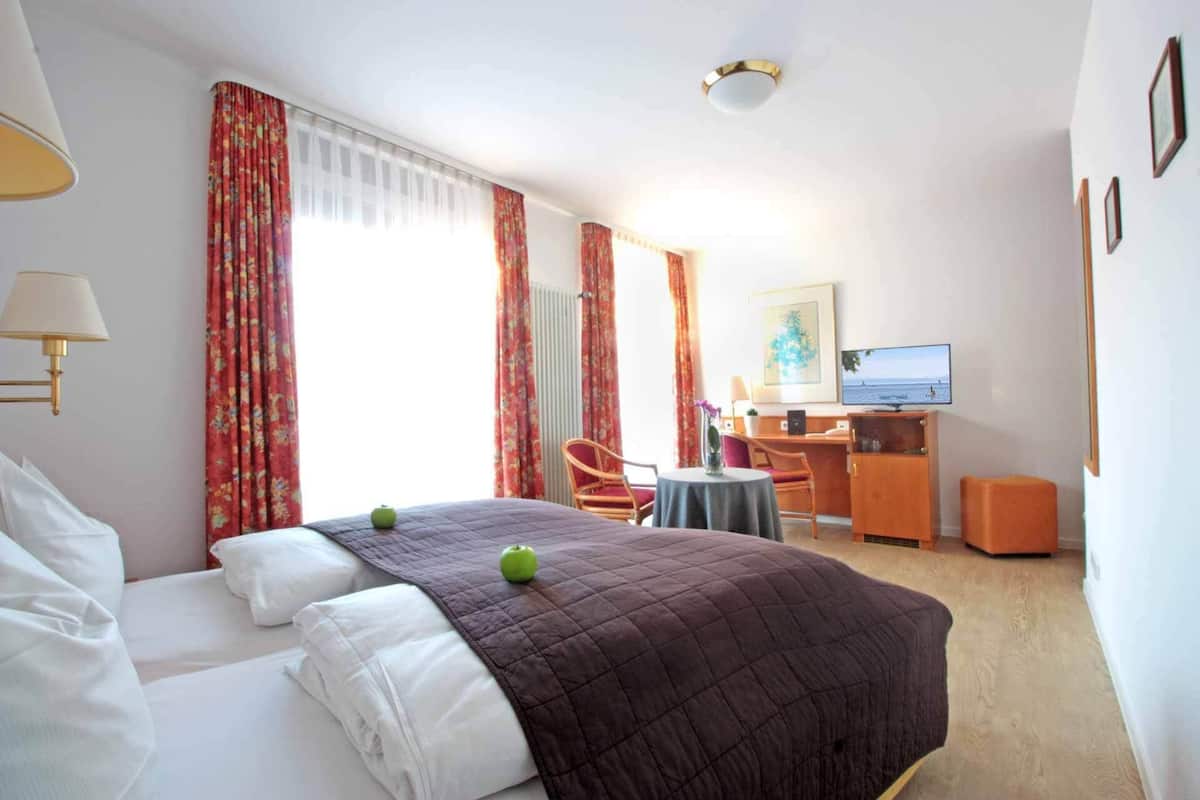 A hotel room with a bed, a desk, a chair, a TV, and a window with curtains.