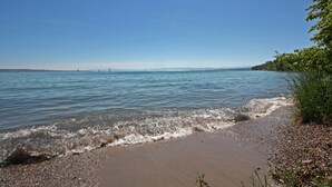 A beach with clear blue water, pebbles, and greenery. - Schiff am See (Konstanz)