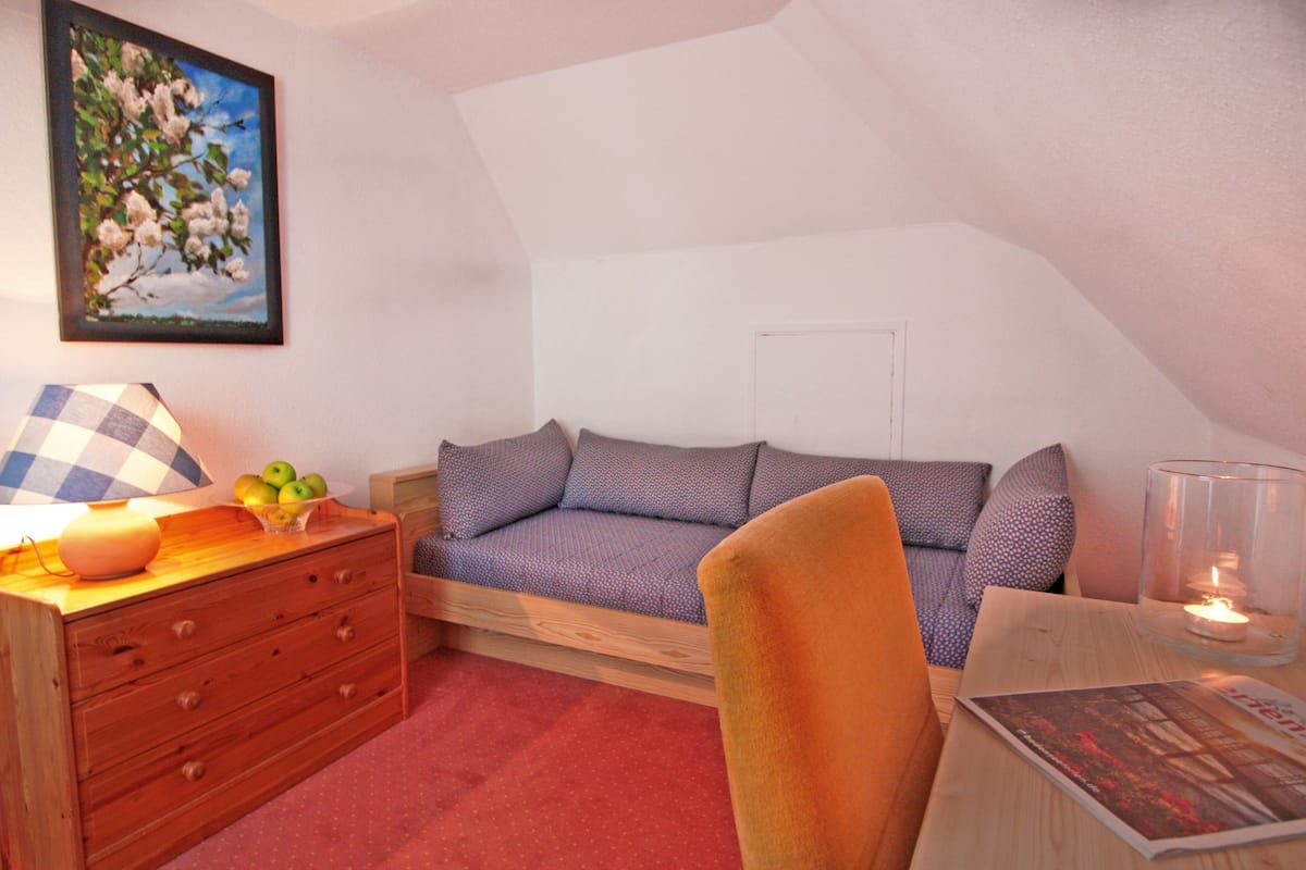 A cozy room with a wooden dresser, a blue and white patterned sofa, a clear glass candle holder, and a framed picture on the wall.