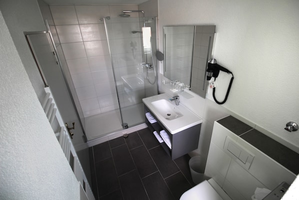 Un baño moderno con ducha de vidrio, lavamanos blanco y espejo sobre él.