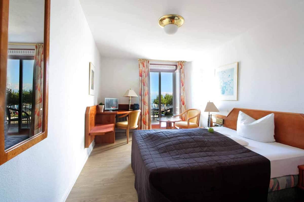 A hotel room with a bed, desk, chair, and a view of the outdoors.