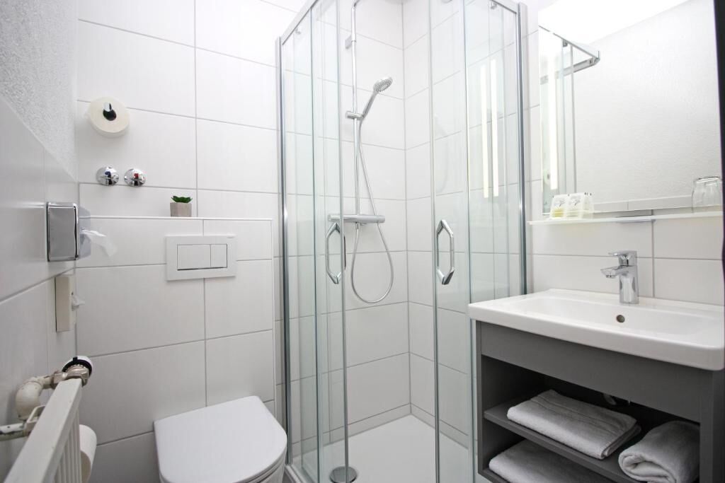 A modern bathroom with a glass-enclosed shower, a white toilet, and a vanity with a sink and towel rack.