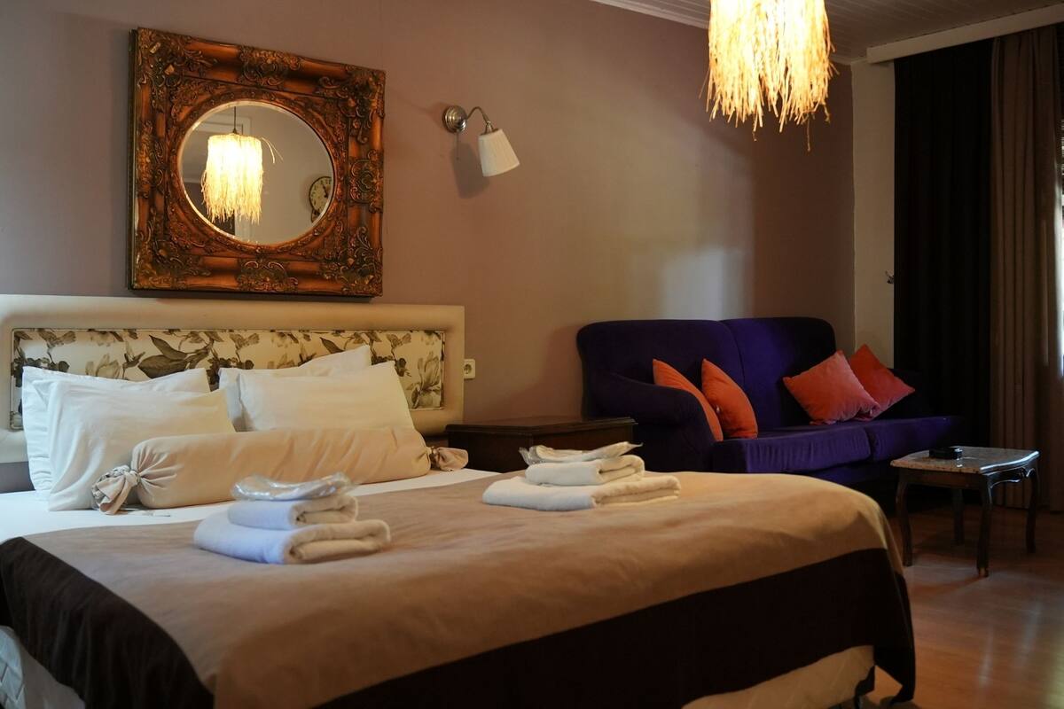 Une chambre d’hôtel avec un grand lit, un canapé, un miroir et un lustre.