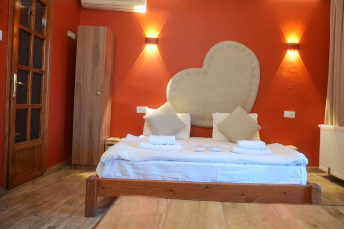 Une chambre avec un lit en bois, deux lampes fixées au mur et une grande décoration en forme de cœur accrochée au mur.