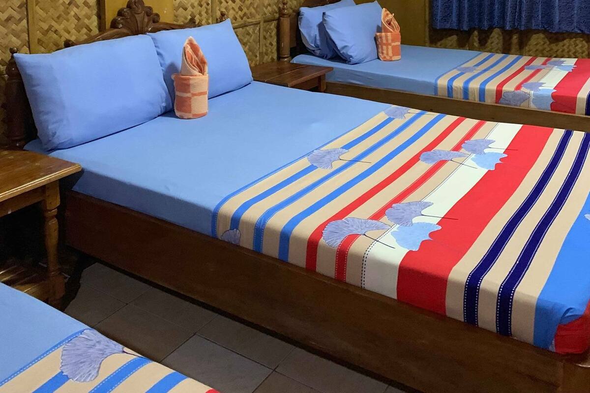 Habitación de hotel con dos camas, cabecero de madera, un panel decorativo en la pared, cortina azul y una mesita.