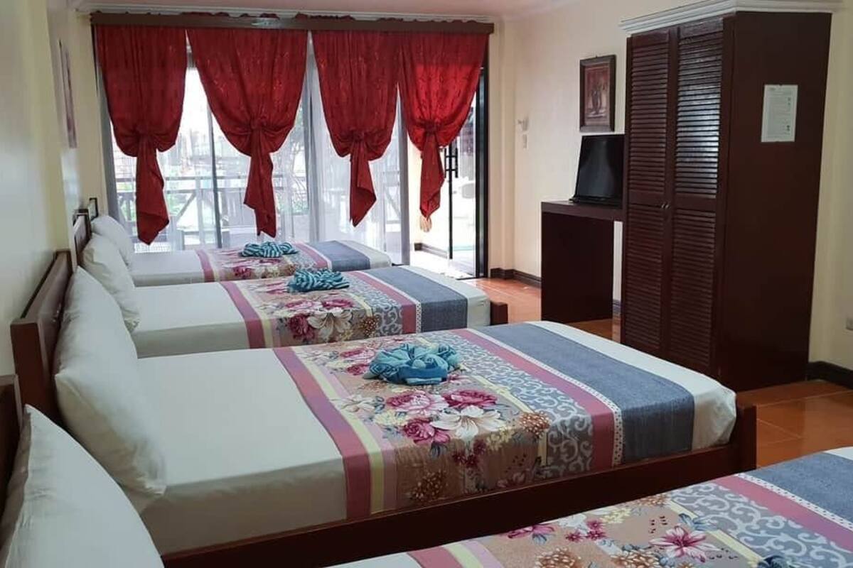 Una habitación de hotel con dos camas, cortinas rojas, un televisor y un armario.