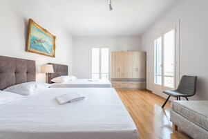 Quarto de hotel com duas camas, um guarda-roupa, uma cadeira e um quadro na parede.