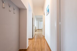 Um corredor estreito com piso de madeira, paredes brancas e uma porta no final que dá para outro quarto.