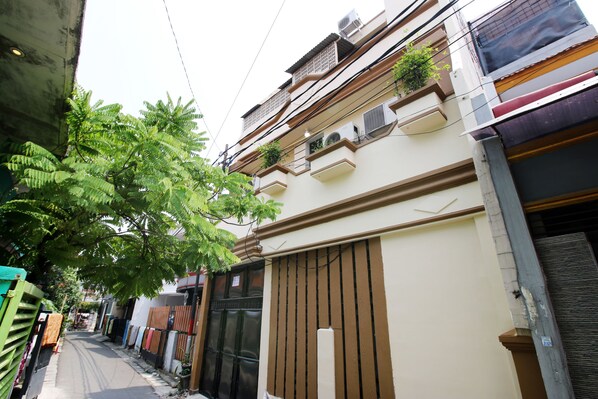 A narrow street with buildings on both sides, featuring balconies with plants and air conditioning units. - Kamar Keluarga Syariah Johar Baru (Jakarta)