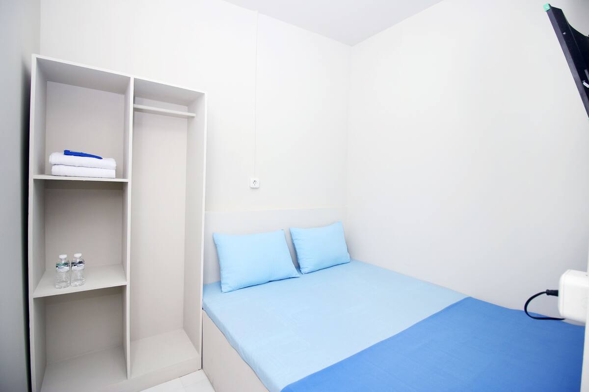 A room with a bed, a wardrobe, and a shelf with bottles.