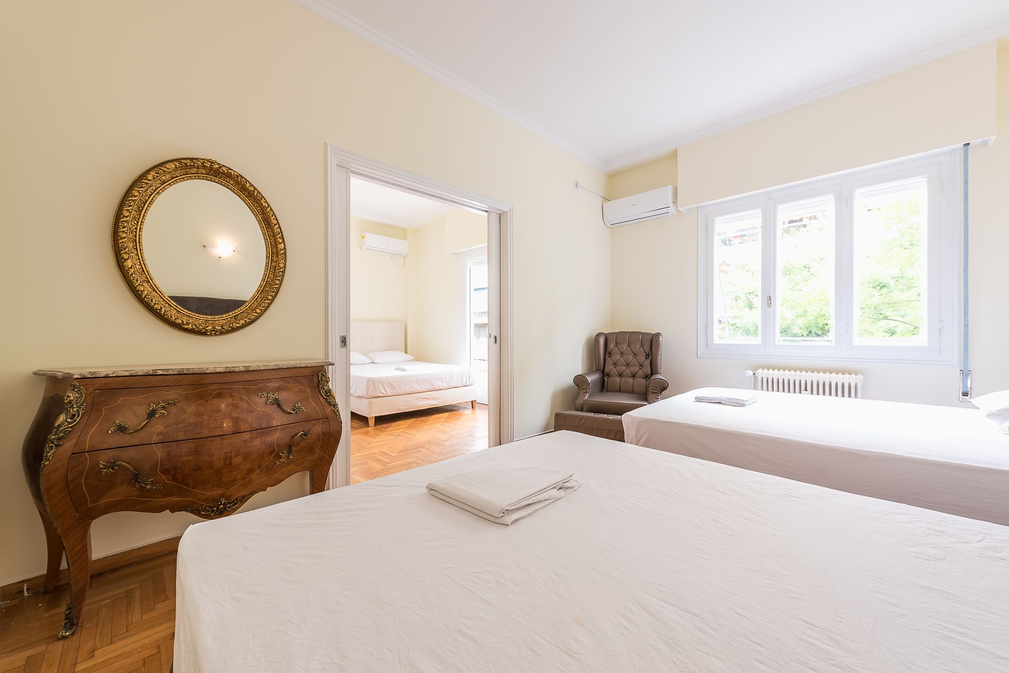 A bedroom with two beds, a wooden dresser, a mirror, and a window with a view.