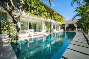 A modern poolside area with a clear pool, lounge chairs, and a covered seating area. - Villa Puro Blanco (Canggu)