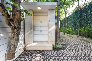 Una entrada cerrada con una puerta blanca, decoraciones de estrellas y un camino empedrado que lleva a una zona verde exuberante.