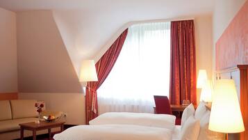 A hotel room with two beds, a sofa, a small table with a vase of flowers, and a window with curtains.