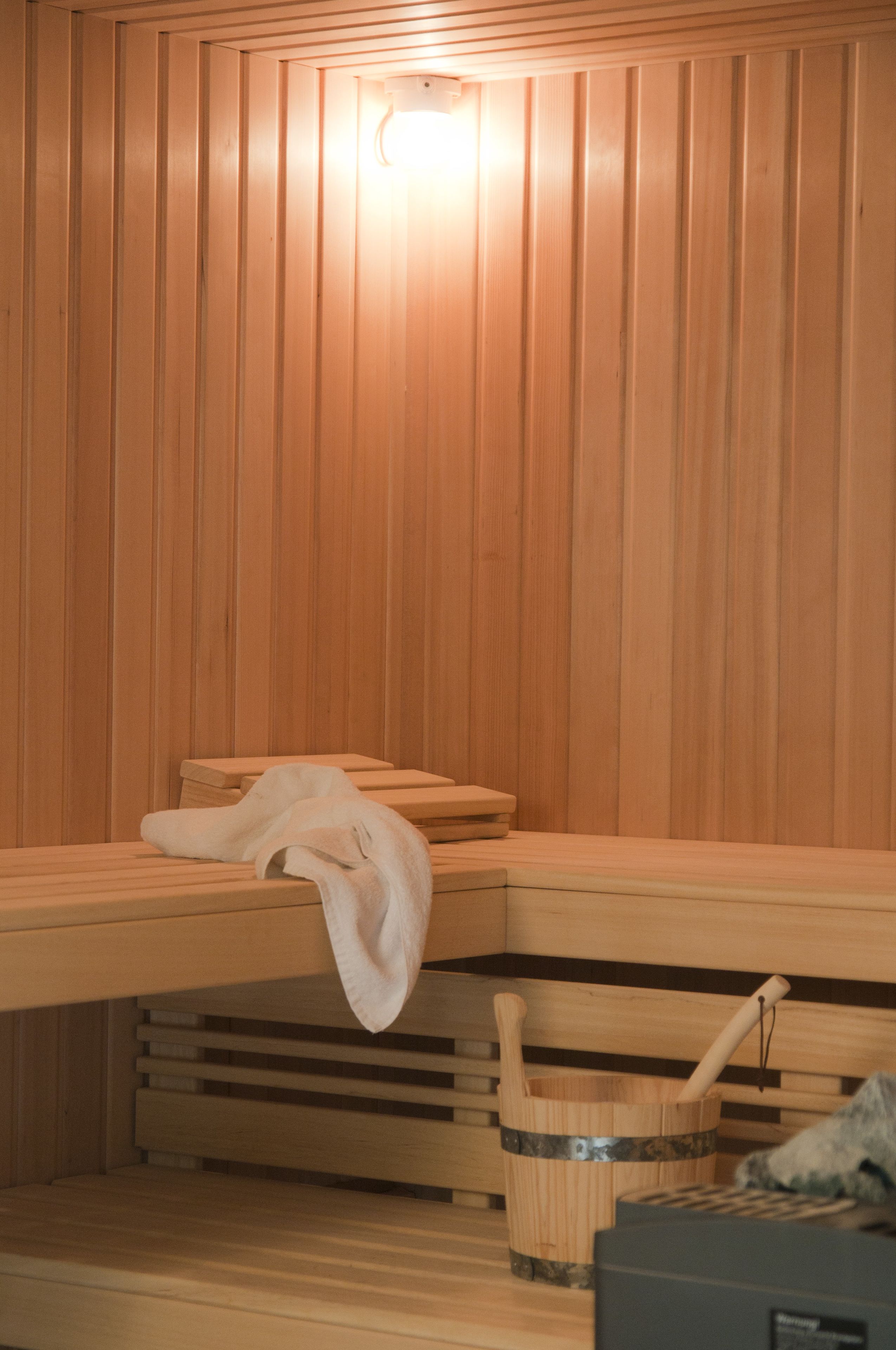 Ein Saunaraum mit Holzbänken, einem Handtuch und einem Holzwaschbecken mit Bürste.