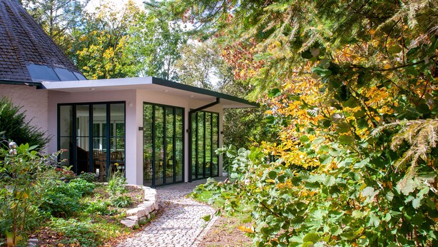 Ein modernes Haus mit überdachter Terrasse, umgeben von üppigem Grün und Bäumen.
