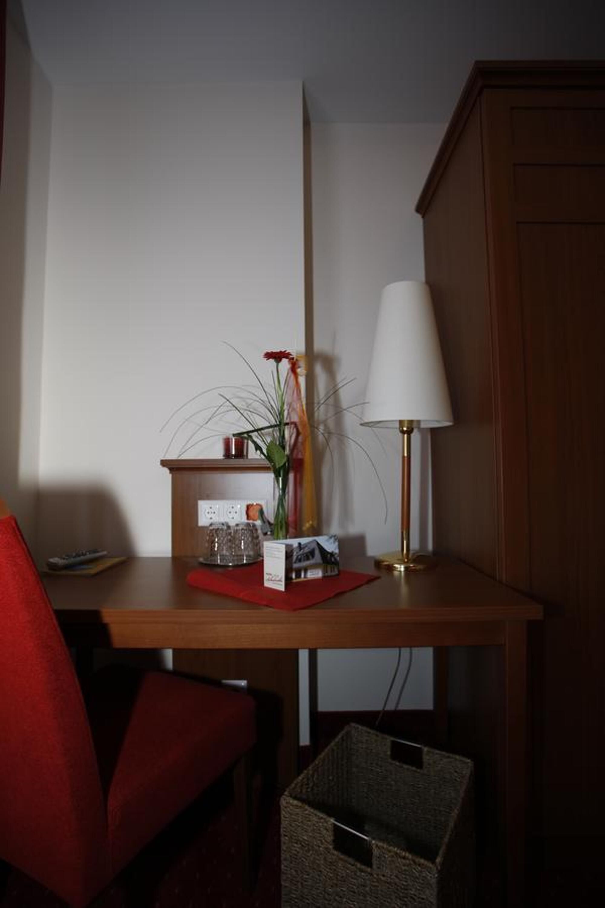 A small wooden table with a lamp, a vase with a flower, and a red placemat.