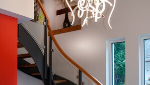 Eine moderne Treppe mit Holzboden und schwarzen Geländern, die zu einem Raum mit großem Fenster und einer außergewöhnlichen Leuchte führt.