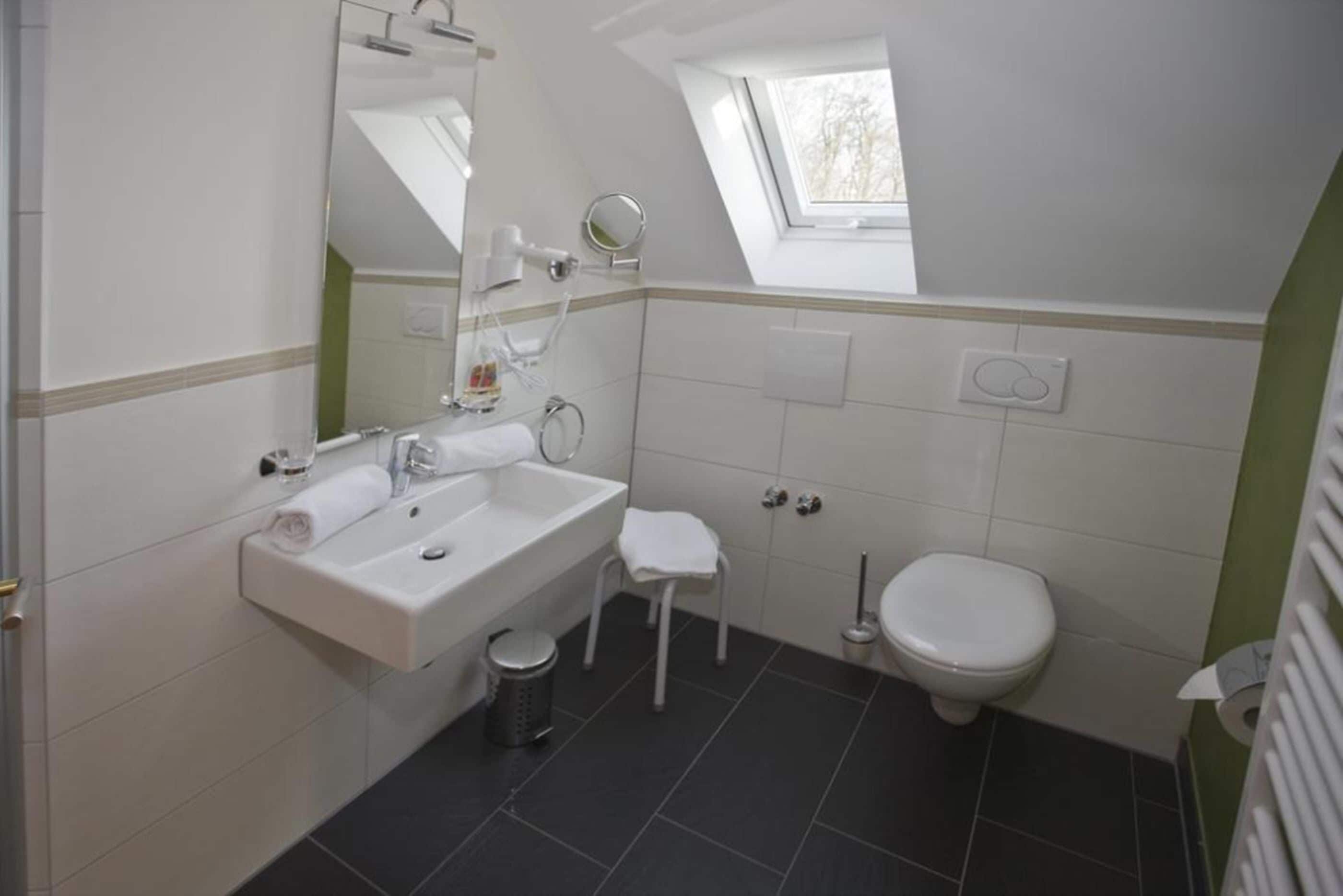 Een moderne badkamer met een wit wastafelmeubel, spiegel en toilet. Er staat een klein krukje en een prullenbak.