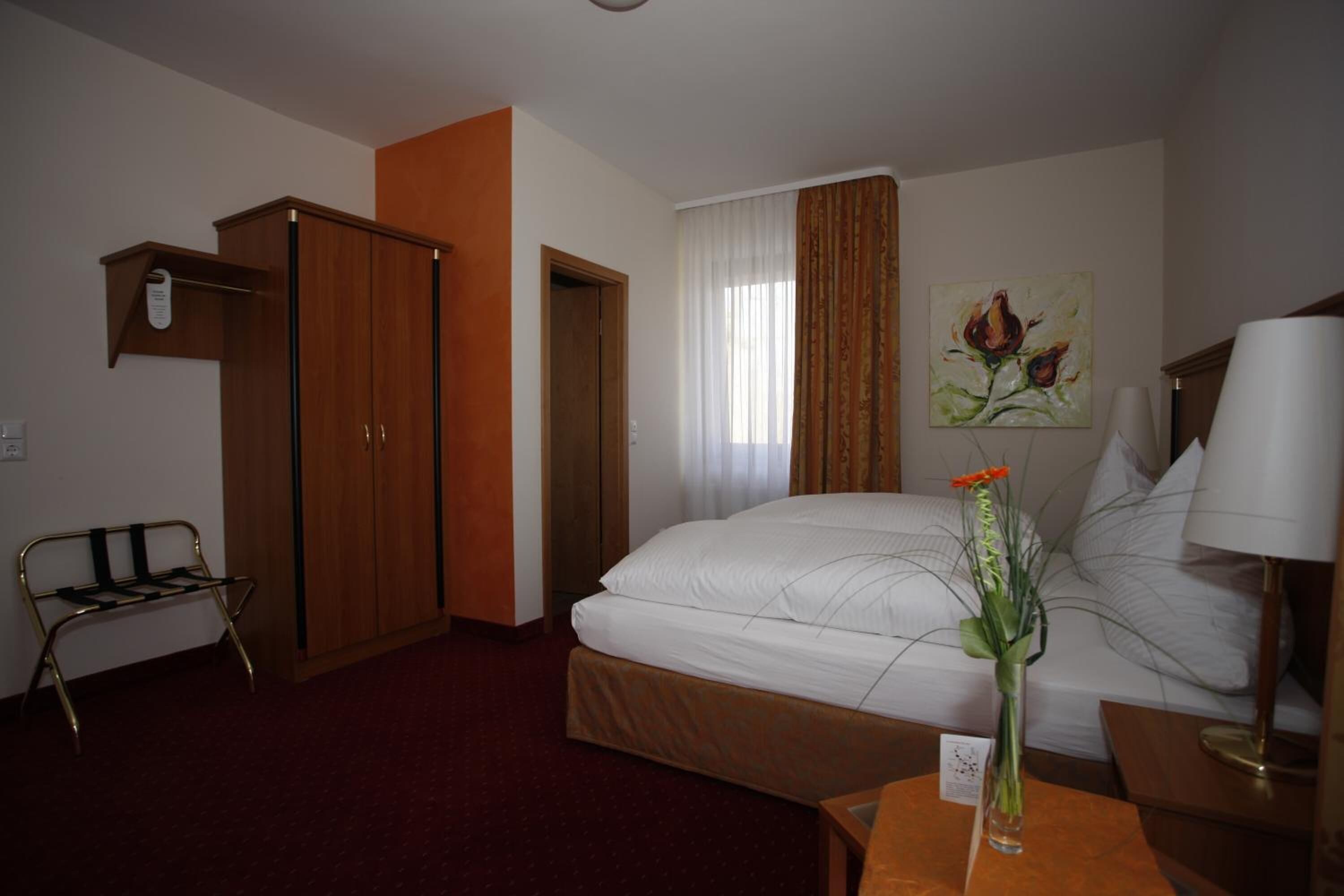 Ein Hotelzimmer mit Bett, Schreibtisch, Stuhl, Kleiderschrank und einem Bild an der Wand.