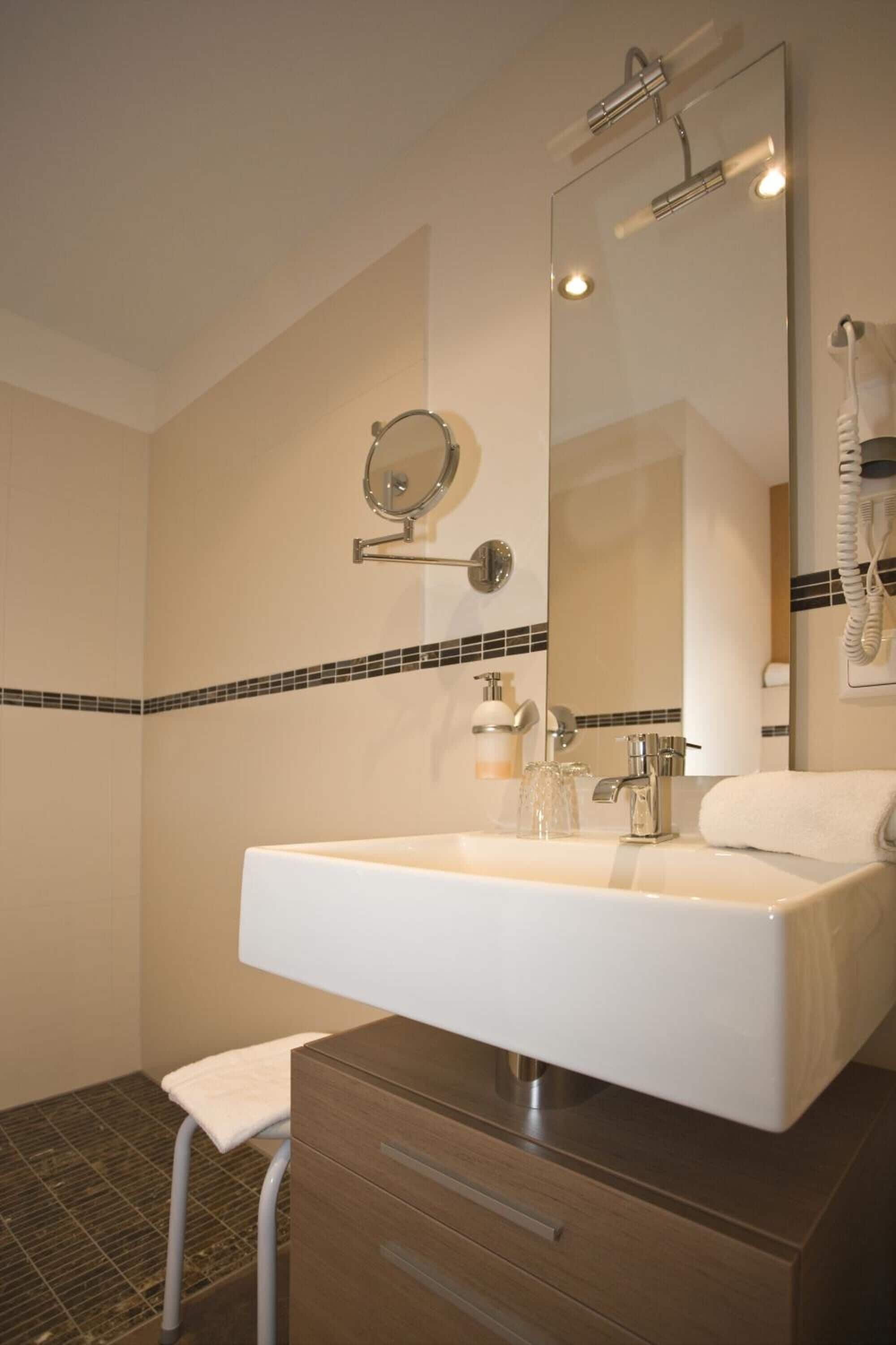 Un baño con un espejo grande, un lavabo blanco, una toalla y un taburete pequeño.