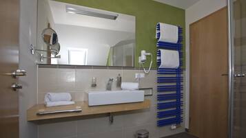 Ein Badezimmer mit Waschbecken, Spiegel, Handtuchhalter und Duschbereich.